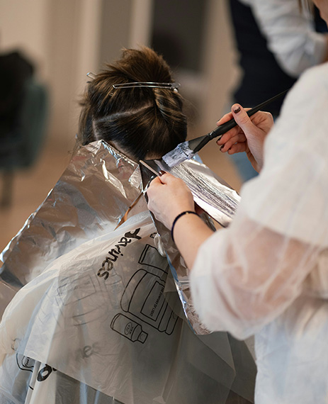 Mujer aplicando tinte en el cabello de otra mujer utilizando placas de papel de aluminio.
